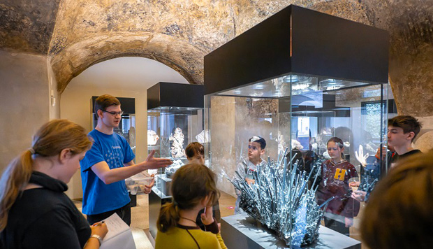 Student mit Schülern vor einer Vitrine mit einem Mineral