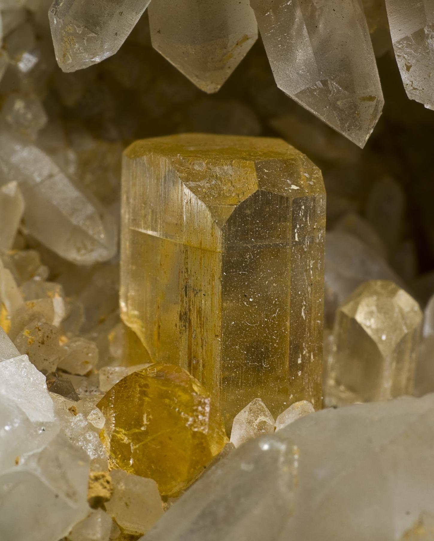 ein weingelber Topaskristall in der Form eines Briefkuverts sitzt in einer Kristallhöhle aus weißem Bergkristall