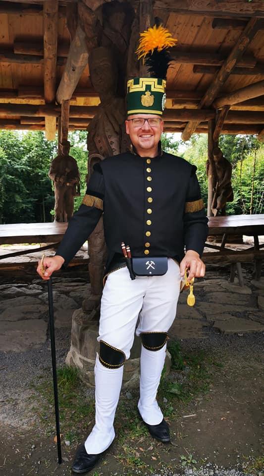 Herr Ittershagen trägt einen bergmännischen Habit. Das ist eine Uniform mit weißen Hosen und schwarzem Bergkittel. Dazu ein grüner Hut mit Feder daran.